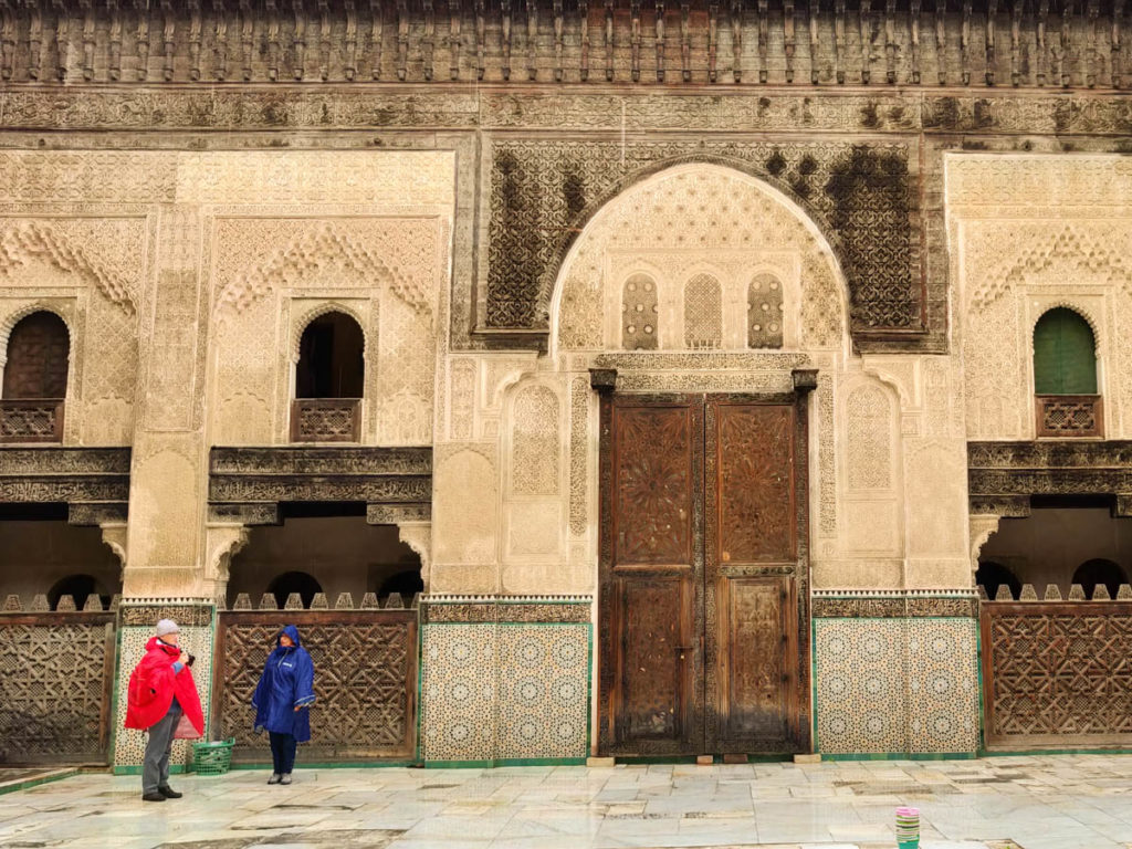 Courtyard of the Madrasa Bou Inania with two people in  raincoats