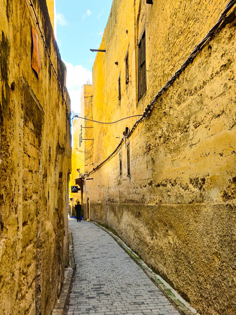 narrow lane between yellow walls, man in the distance. Medina of Fes, one of the things to see in Fes