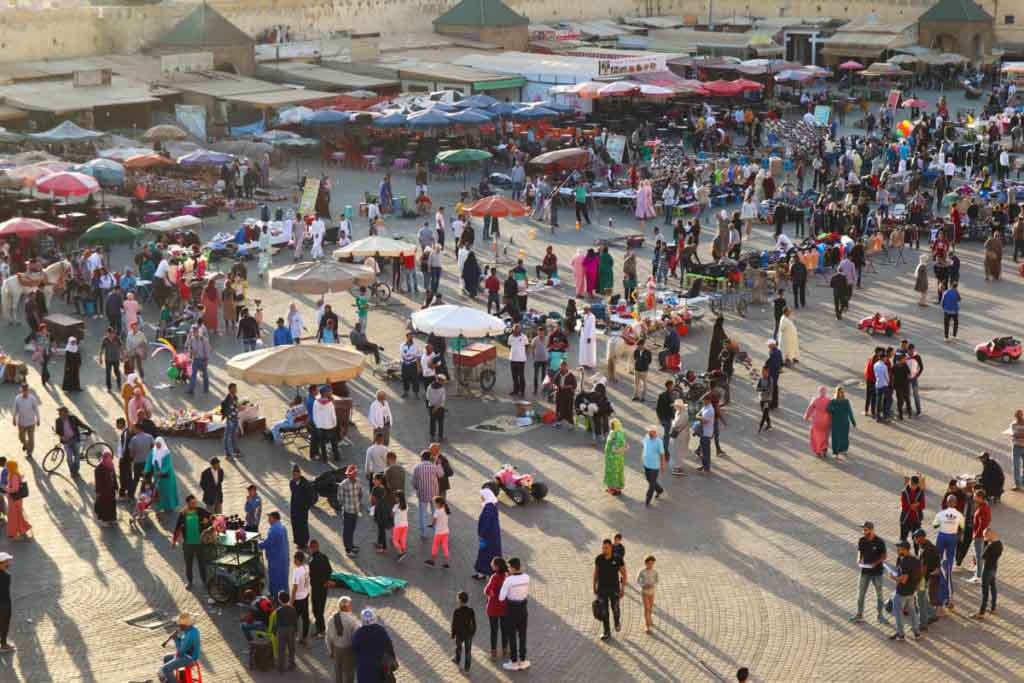 Square full of people and umbrellas in the afternoon sun. Place el hedim, Meknes