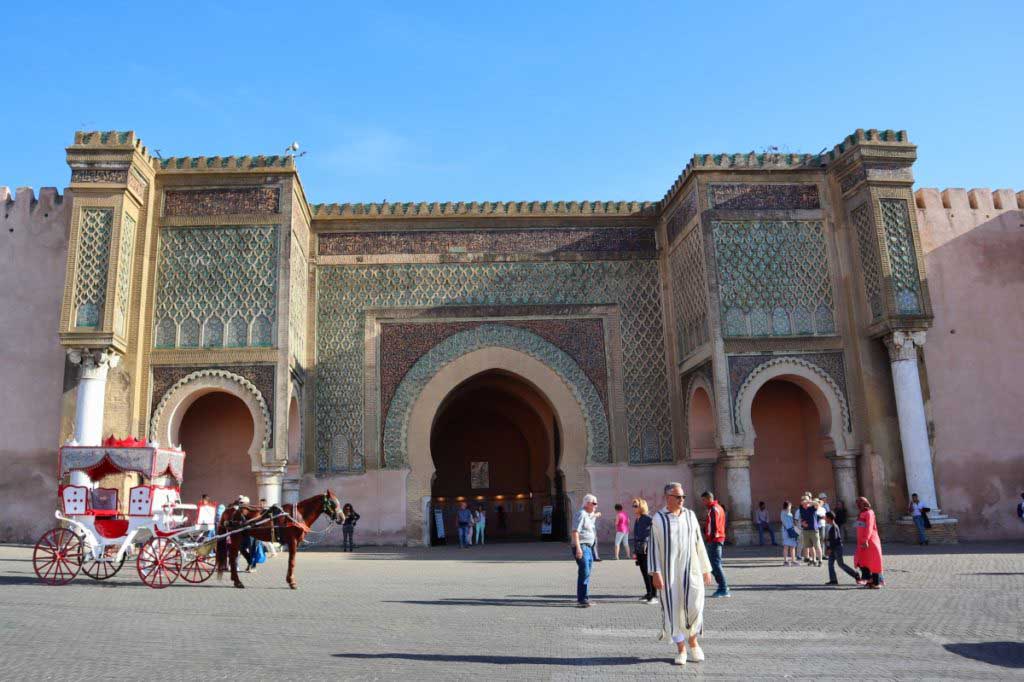 Big city gate in Meknes, one of the imperial cities of Morocco, people crossing the street, a horse and carriage waiting for customers