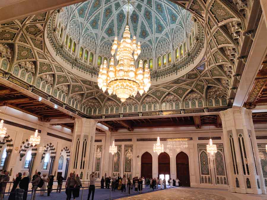 the most beautiful mosque in the world that non-Muslims are allowed to visit from the inside, Sultan Qaboos mosque in Muscat. bit chandelier, decorated roof, people taking photos