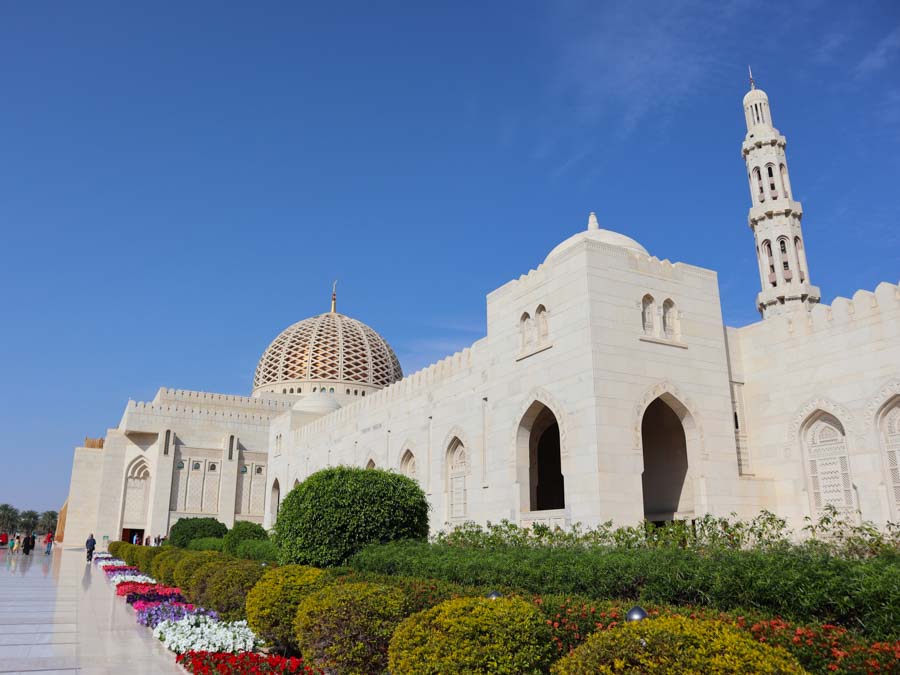 Sultan Qaboos grand mosque with big dome in the background and colourful flower beds in the foreground. One of the best places to visit in Oman