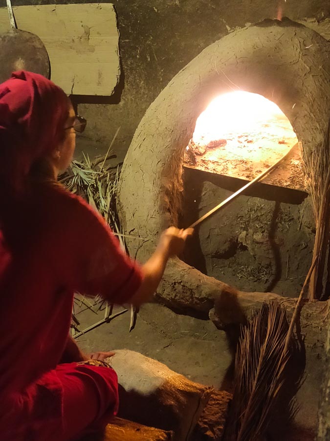 Moroccan woman infront of traditional clay oven baking bread