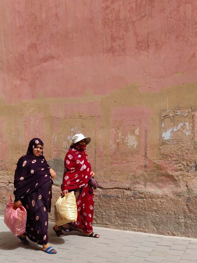 2 Moroccan women in traditional dresses walking along a wall