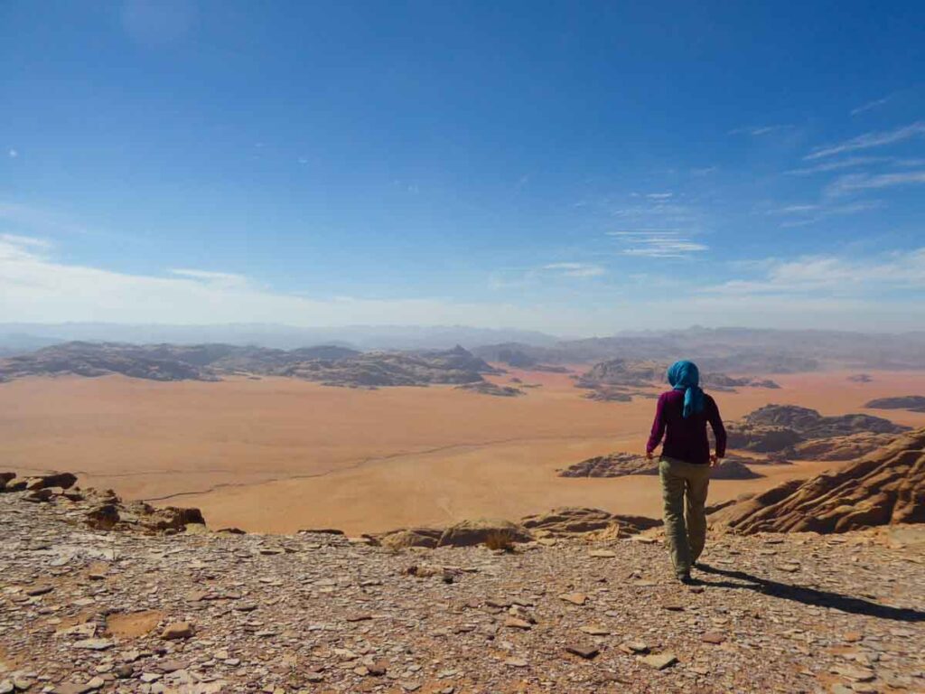 Woman at the edge of a cliff overlooking red and orange valley below. View of Saudi Arabia from Wadi Rum. travel guide to Jordan