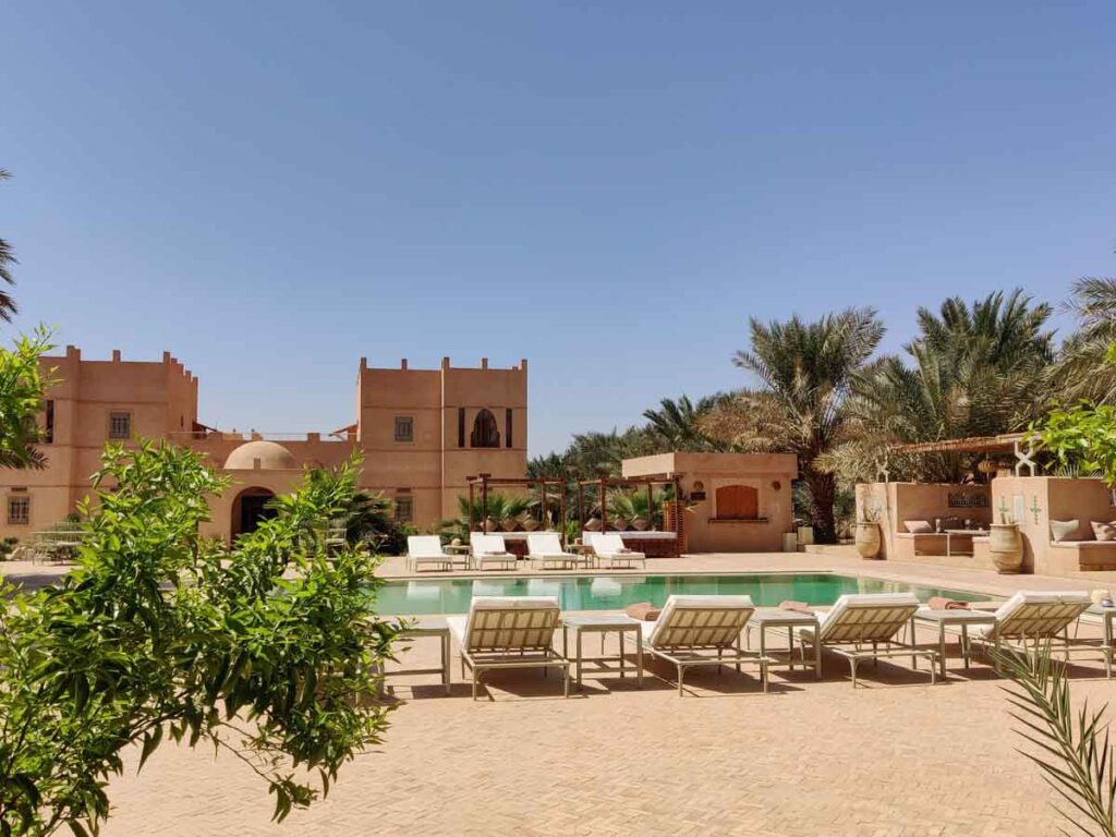 Pool mit vielen Liegen und Grünpflanzen im Riad Serai in Merzouga. Bestes Hotel in Merzouga